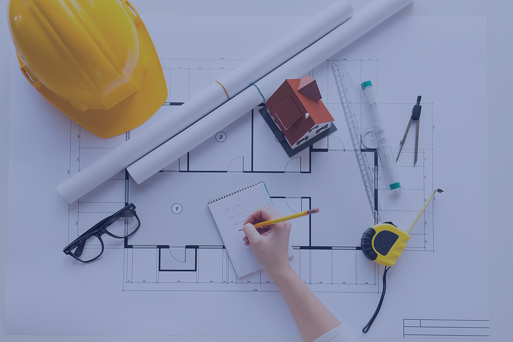 Engineer's hand writing on pad with hard hat and building plans